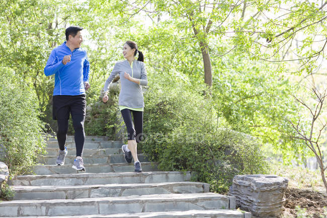 Mature chinese couple running on stairs in park — Stock Photo