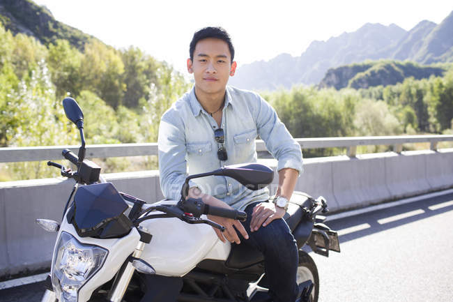 Китаец сидит на мотоцикле и смотрит в камеру — стоковое фото