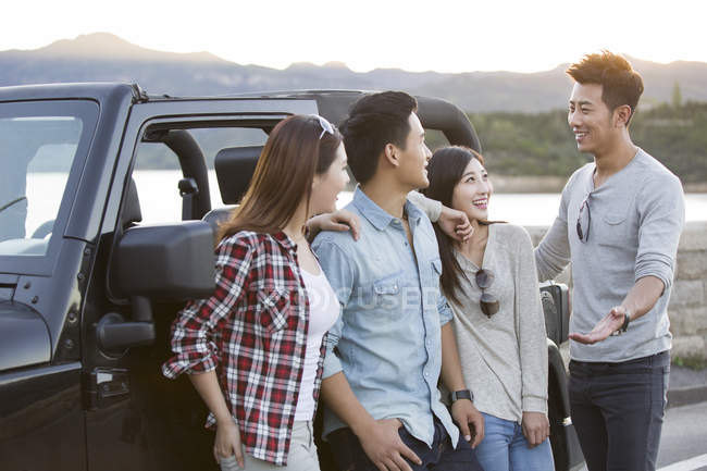 Amigos chinos charlando delante del coche en los suburbios - foto de stock