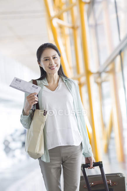 Mature chinese woman walking in airport with suitcase — Stock Photo