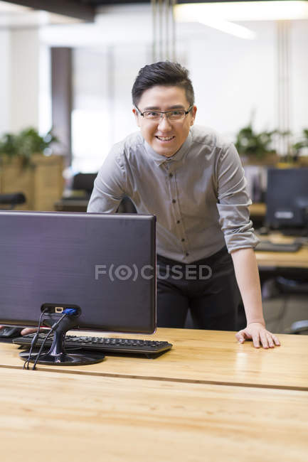 Chino trabajador de TI masculino apoyado en el escritorio en la oficina - foto de stock