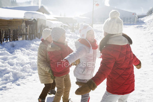 Niños de edad elemental chinos jugando en la nieve en la aldea - foto de stock