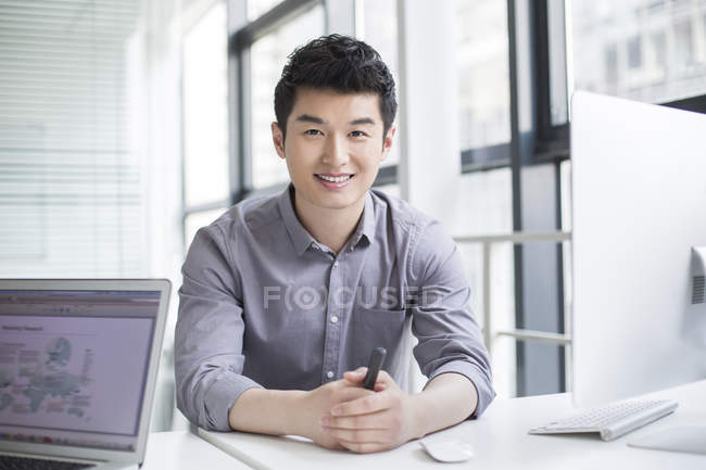 Chinese businessman sitting in office with hands clasped — Stock Photo