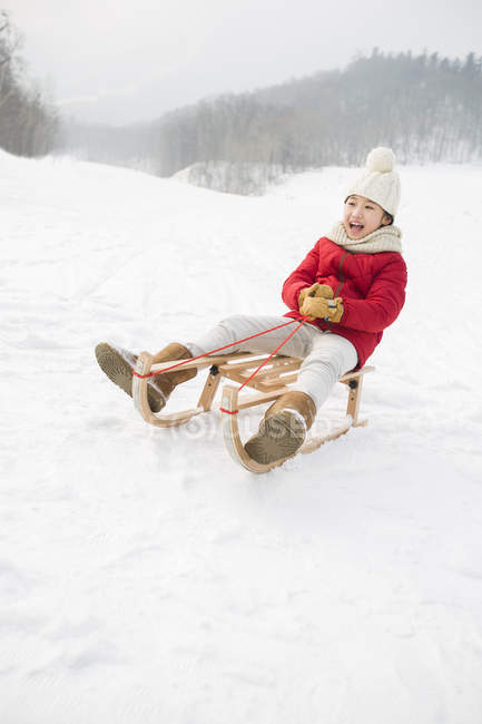 Menina chinesa deslizando no trenó em tempo nevado — Fotografia de Stock