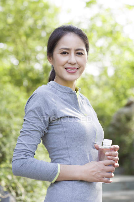 Femme chinoise mature en vêtements de sport tenant bouteille avec de l'eau — Photo de stock