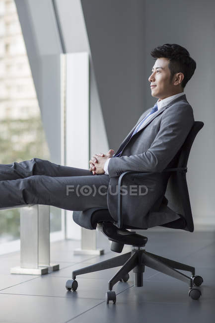 Китайский бизнесмен смотрит в окно в офисе — стоковое фото