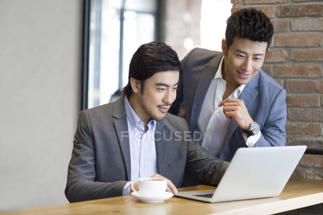 Los hombres asiáticos usando el ordenador portátil en la cafetería - foto de stock