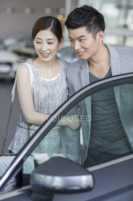 Chinese couple looking at car in showroom — Stock Photo
