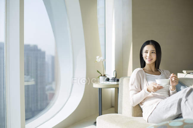 Chinese woman eating porridge on sofa in home interior — Stock Photo