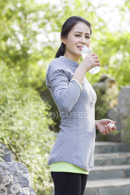 Зрелая китаянка в спортивной одежде пьет воду — стоковое фото