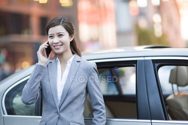 Chinese woman talking on phone in front of car — Stock Photo