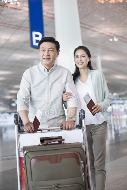 Зрелая китайская пара, идущая в аэропорт с чемоданом — стоковое фото