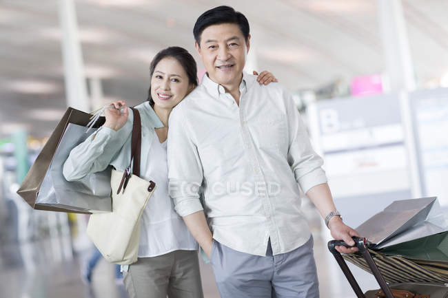 Mature couple chinois debout à l'aéroport avec des sacs à provisions — Photo de stock