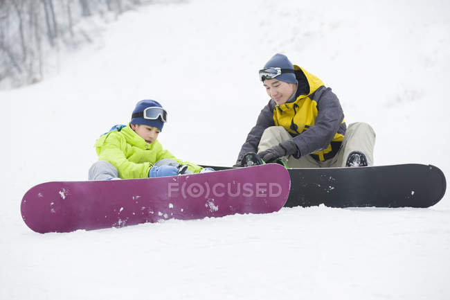 Chino padre e hijo sentado con tablas de snowboard en la nieve - foto de stock