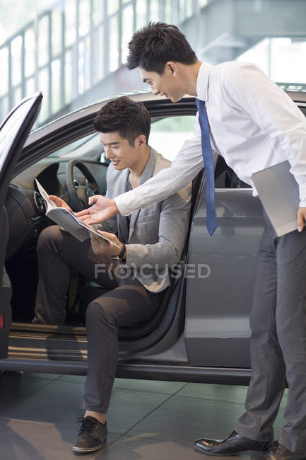 Chinese car dealer helping client choosing car in showroom — Stock Photo