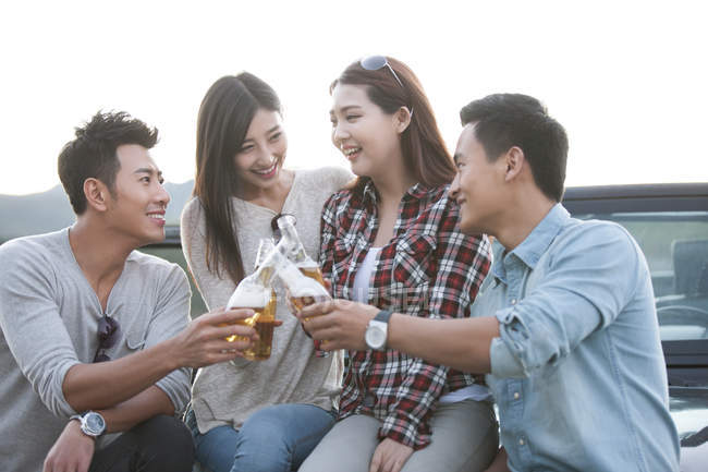 Chinese friends sitting on car with beer — Stock Photo