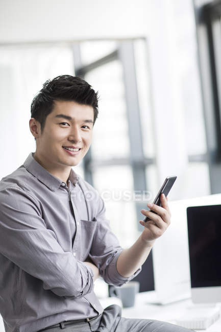 Chinese businessman holding smartphone in office — Stock Photo