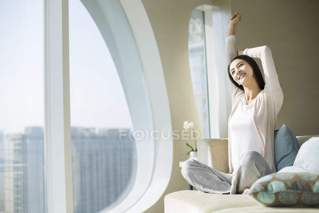 Femme chinoise étirant sur le canapé le matin à l'intérieur de la maison — Photo de stock
