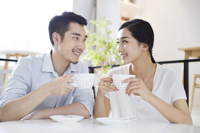 Pareja china sentada con tazas de café en la cafetería - foto de stock