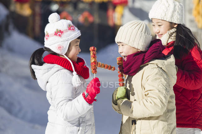 Chinese children eating candied haws at winter — Stock Photo