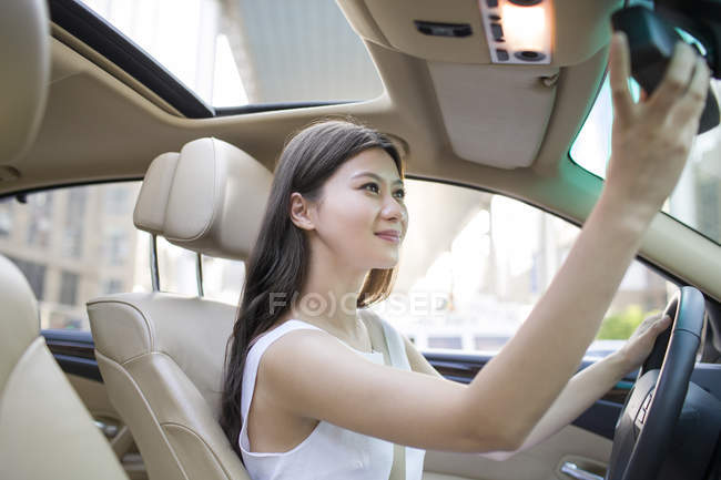 Китаянка регулирует зеркало в машине — стоковое фото