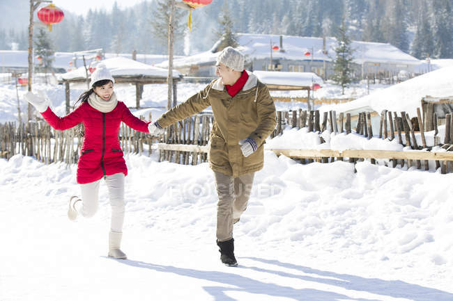 Casal chinês de mãos dadas e correndo na neve — Fotografia de Stock