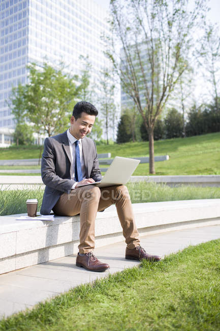 Chinese businessman using laptop in green area — Stock Photo