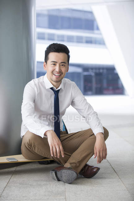 Uomo d'affari cinese seduto su skateboard al parcheggio — Foto stock