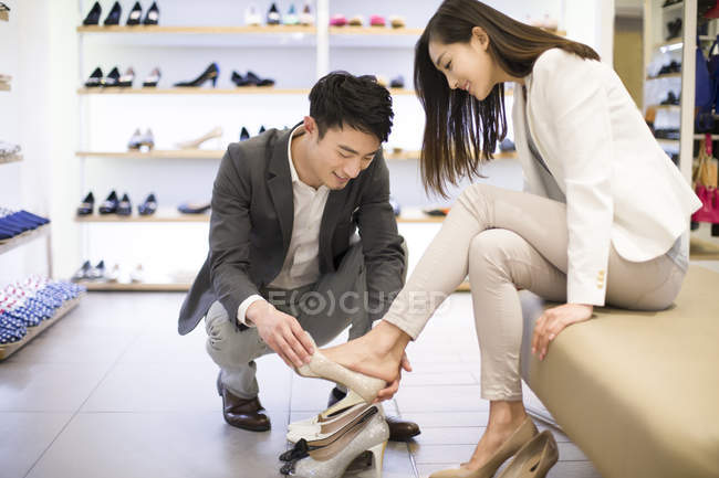 Hombre chino con mujer eligiendo y probando zapatos en la tienda - foto de stock
