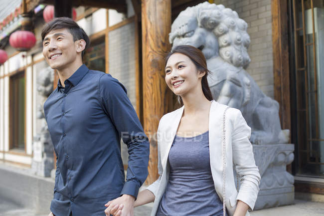 Chinese couple holding hands in front of sculpture — Stock Photo