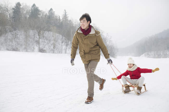 Chinese father running and pulling daughter on sled — Stock Photo
