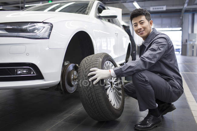 Mecánico auto chino que sostiene la rueda del coche en taller - foto de stock