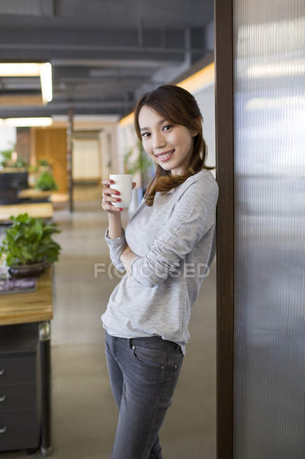 Mulher chinesa de pé com xícara de café no escritório — Fotografia de Stock