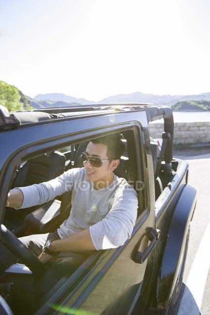 Hombre chino conduciendo coche y sonriendo - foto de stock