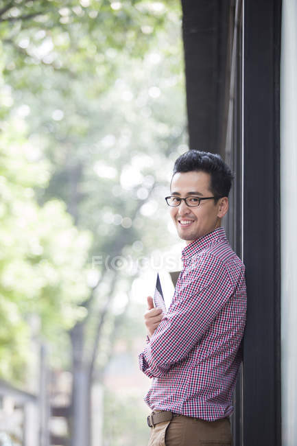 Средний взрослый китайский мужчина держит цифровой планшет и улыбается — стоковое фото