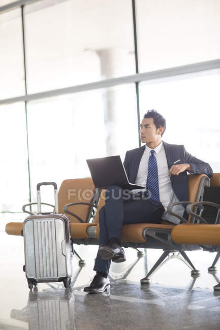 Uomo d'affari cinese seduto con laptop nella sala d'attesa dell'aeroporto — Foto stock