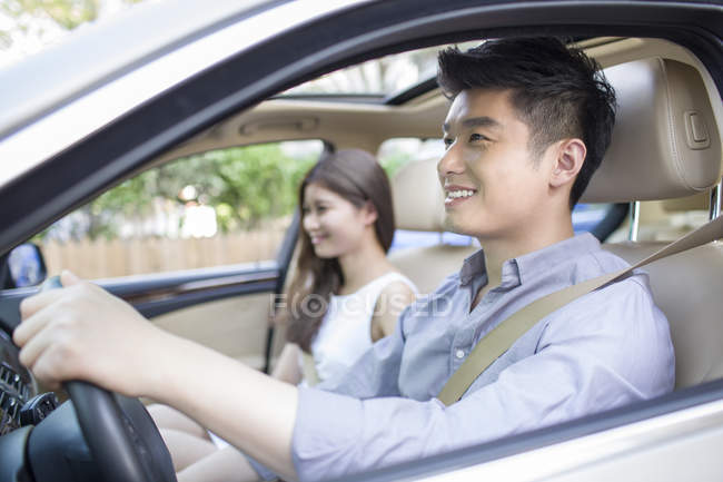 Pareja china sentada en coche y sonriendo - foto de stock