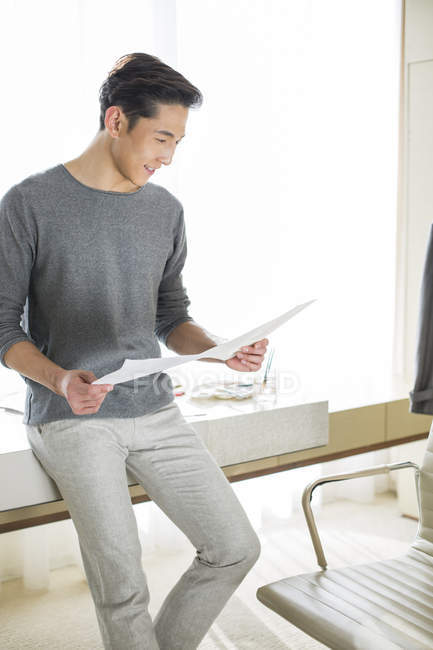 Chinese designer sitting on table and looking at sketches — Stock Photo