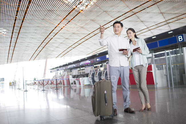 Pareja china madura parada en el aeropuerto con entradas - foto de stock