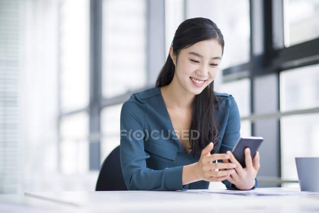 Китайская предпринимательница использует смартфон в офисе — стоковое фото