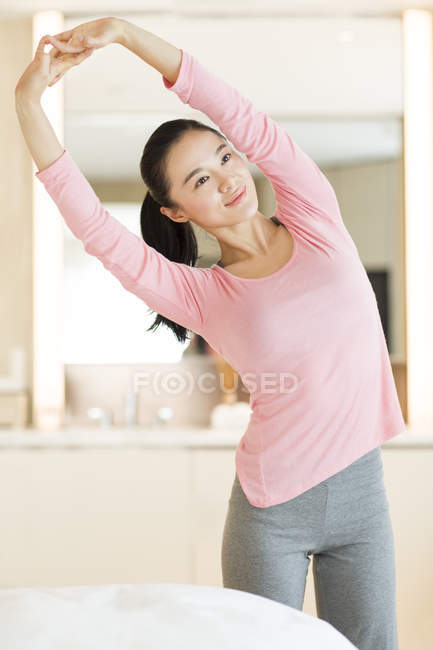 Китаянка в розовой спортивной одежде растягивается в спальне — стоковое фото