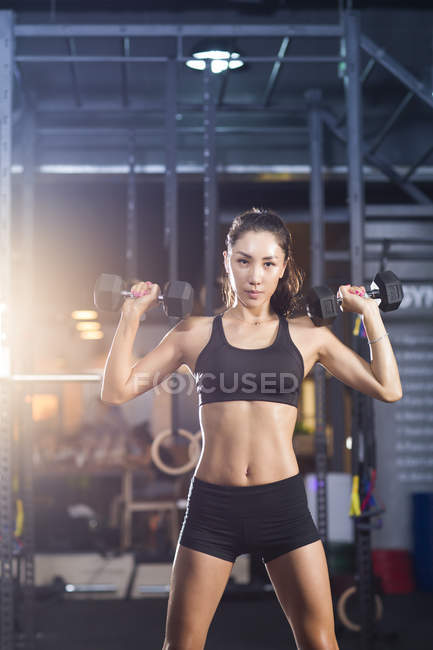 Chinese woman lifting dumbbells at gym — Stock Photo