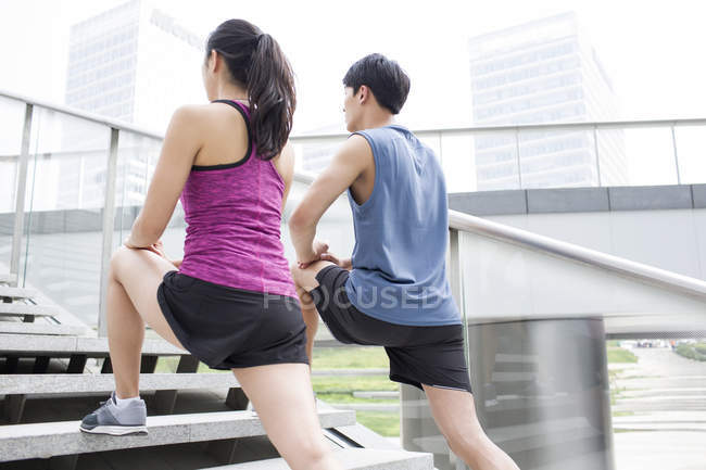 Chinese couple stretching legs on stairs — Stock Photo