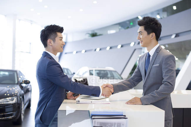 Uomo cinese stringere la mano con rivenditore di auto in showroom — Foto stock