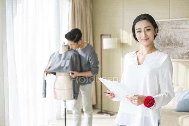 Китайская модельер держит эскизы, пока мужчина работает — стоковое фото