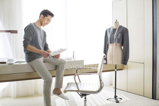Chinese fashion designer sitting on table and looking at sketches — Stock Photo
