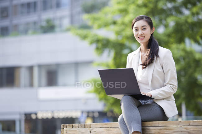 Empresária chinesa sentada com laptop no banco — Fotografia de Stock