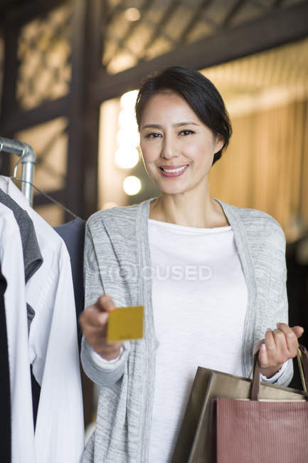 Mature Chinese woman standing with credit card in clothing store — Stock Photo