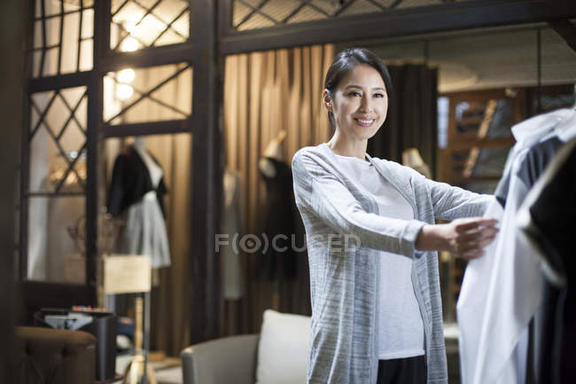 Mature chinois boutique propriétaire vérifier vêtements sur rack — Photo de stock