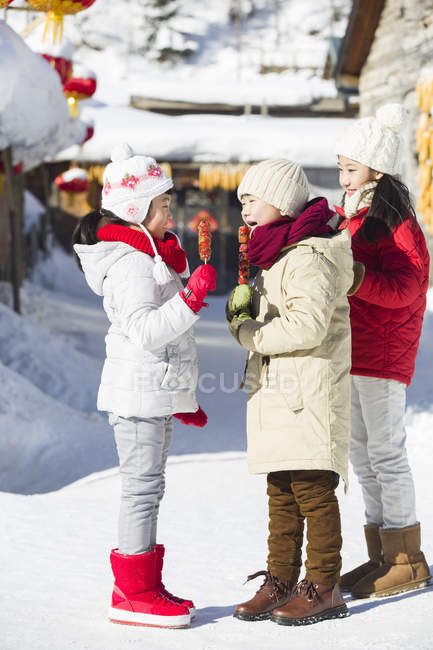 Chinese children eating candied haws in snowy village — Stock Photo